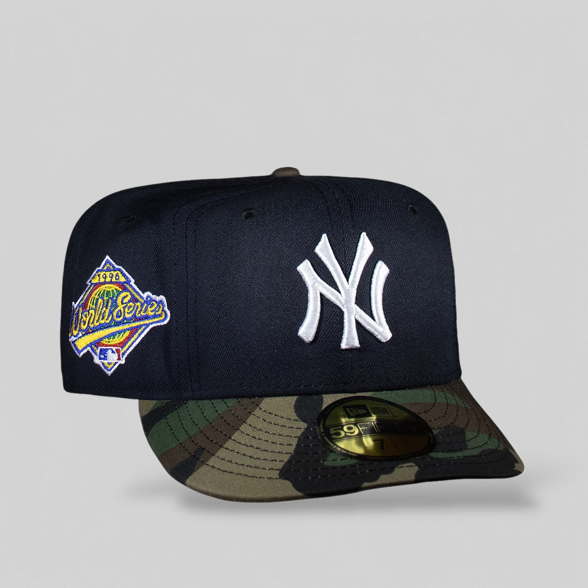A fitted cap with camouflage pattern on the visor, navy blue body, and New York Yankees logo on the front, with a 1996 World Series patch on the side.